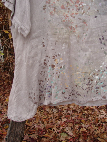 Barclay Lightweight Linen Tea Time Top Fall Rain Sand Size 1 draped on a wooden post outdoors. Features a flowy A-line shape, varying hemline, and three-quarter sleeves with a natural pattern.