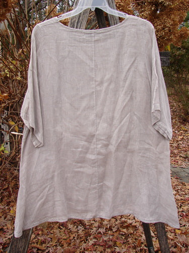 Barclay Lightweight Linen Tea Time Top Fall Rain Sand Size 1 displayed on a hanger, showcasing its flowy A-line shape, rounded neckline, varying hemline, and three-quarter length sleeves against an autumnal outdoor backdrop.