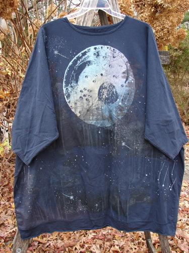Barclay Cotton Lycra Flutter Hem Dolman Pullover Centered Ink OSFA, featuring a circular moon and star graphic, hangs on a clear plastic hanger outdoors, showcasing its boxy shape and three-quarter sleeves.