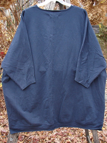 The Barclay Cotton Lycra Flutter Hem Dolman Pullover Centered Ink OSFA features a loose fit, drop dolman shoulders, three-quarter sleeves, and a fluttered hemline, displayed against a natural outdoor setting.