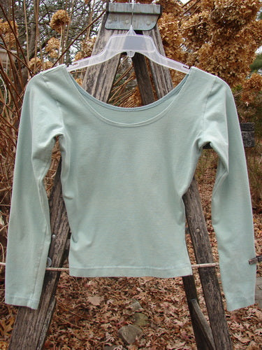 1994 Cotton Lycra Ballerina Layering Top Unpainted Menthe Smaller Size 1 hangs outdoors on a plastic hanger, showcasing its long sleeves, tapering waist, and ballerina neckline. Perfect for snug, stylish layering.