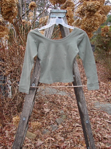 1994 Cotton Lycra Ballerina Layering Top Unpainted Seaweed Smaller Size 1, shown on a clear hanger against an outdoor autumn backdrop, highlighting its fitted shape, ballerina neckline, and substantial stretch fabric.