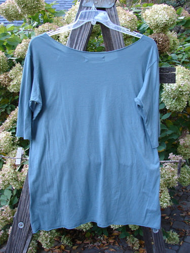 Barclay Batiste Raw Edge Tee Top Unpainted La Mer Size 1: A blue shirt on a wooden rack, featuring lovely three-quarter length sleeves, a soft neckline, roll-over edgings, and a slight narrowing lower shape.
