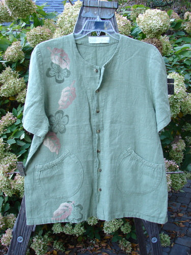 1998 Botanicals Robin's Top: A green shirt with flowers, featuring a smaller back shoulder line, a super A-line shape, and elastic-topped rounded bottom pockets. Perfect buttons and mixed garden theme paint adorn this thick weighted linen top. Bust 46, Waist 48, Hips 50, Hem Circumference 54, Length 27.