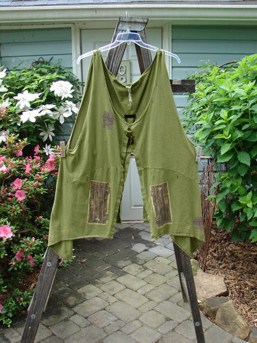 Vintage Blue Fish Clothing: 1993 Holy Vest Mythical Door Olive Size 2 on clothes rack, surrounded by plants and outdoor elements. Reflects BlueFishFinder's ethos of creative freedom and individuality.