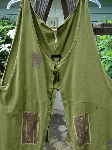 Vintage 1993 Holy Vest Mythical Door Olive Size 2 by BlueFishFinder, hanging on a clothesline. Green overalls with patches, embodying creative freedom and individuality through unique textile patterns.