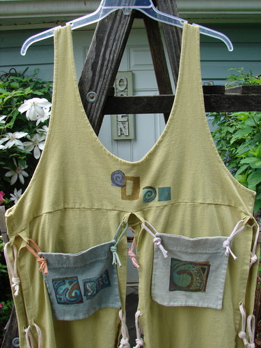 1996 4 Corner Pocket Apron Geo Key Lemon OSFA displayed on a wooden rack. Vintage Blue Fish Clothing piece with unique features like oversized tie-on pockets and empire waistline. Reflects BlueFishFinder's ethos of creative expression through fashion.