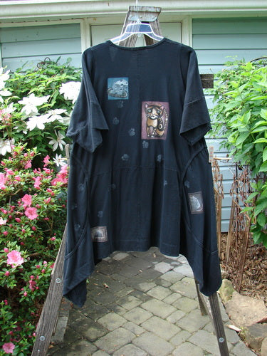 Barclay Double Pocket Bounce Tunic Dress Cat & Mouse Black Size 2 featuring cat and mouse illustrations, oversized front pockets, and a dramatic scooped hemline, worn outdoors on a stone walkway.