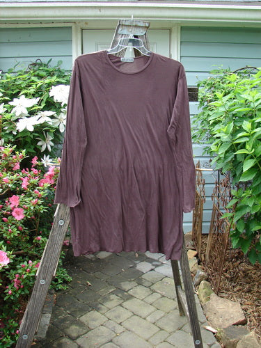 Barclay Batiste Tunic Curve Top Unpainted Red Earth Size 2 draped over a wooden ladder, showcasing its longer sleeves, rounded neckline, and tapered bodice with sweet curly edgings.