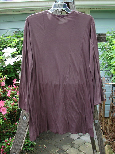 A long-sleeved Barclay Batiste Tunic Curve Top Unpainted Red Earth Size 2, displayed on a wooden pole, highlighting its curvy seams, narrow forearms, and rounded neckline.