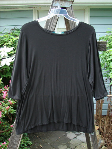 A Barclay Rayon Lycra Basic Top Unpainted Charcoal Size 2 displayed on a hanger, showcasing three-quarter length sleeves, a varying upward scoop front hemline, and a slightly shallow rounded neckline.
