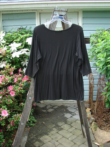 Barclay Rayon Lycra Basic Top Unpainted Charcoal Size 2 displayed on a wooden pole, highlighting its three-quarter length sleeves and varying upward scoop front hemline.