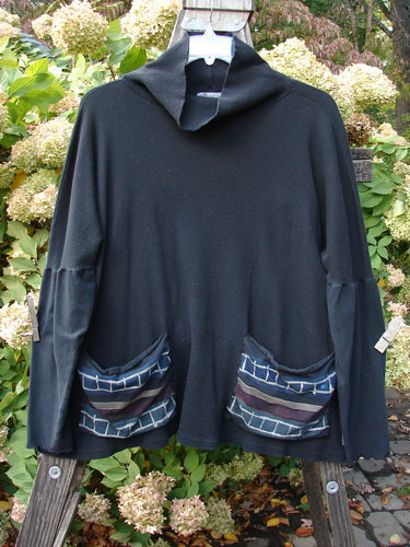 A black shirt with pockets, featuring a floppy double cowl turtleneck, painted patches, and contrasting rib dolmen sleeves. Size 3.