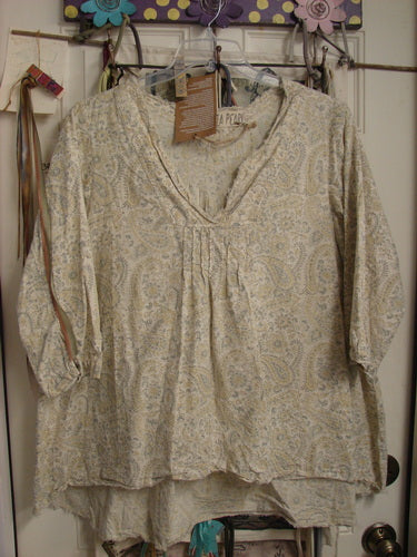 Magnolia Pearl NWT European Cotton Bondi Blouse Fleuri OSFA, featuring pintuck details and flowing three-quarter sleeves, hangs on a door, showcasing its light, paisley-like print and raw-edged V-neckline.