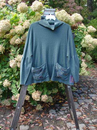 A Barclay Patched Thermal Tie Back Cowl Top in Army, featuring a blue sweater with pockets on a wooden stand.