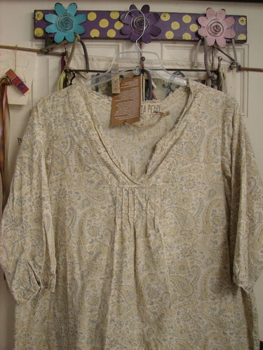 The Magnolia Pearl NWT European Cotton Bondi Blouse Fleuri OSFA, with a paisley print and V-neck, hangs on a decorative wall rack, showcasing its soft blue and yellow pastel block printing.