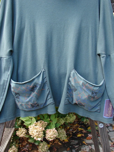A close-up of a Barclay Patched Thermal Tie Back Cowl Top with flower patches and a pocket on a blue shirt.