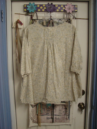 Magnolia Pearl NWT European Cotton Bondi Blouse Fleuri OSFA hangs elegantly on a floral hook, highlighting its paisley print, raw-edged V-neckline, and billowy sleeves, embodying Bluefishfinder.com's vintage charm.