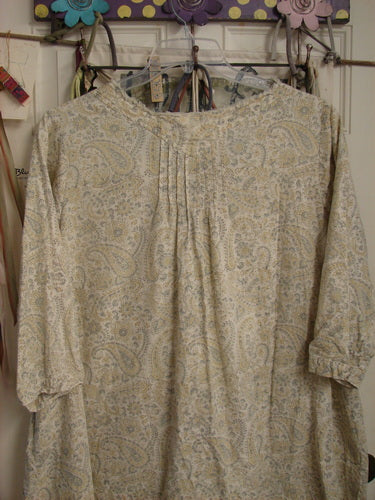 Magnolia Pearl NWT European Cotton Bondi Blouse Fleuri OSFA, featuring a paisley print, raw-edged V-neck, and relaxed three-quarter sleeves, hangs from a decorative rack. Perfect for individualistic style expression.
