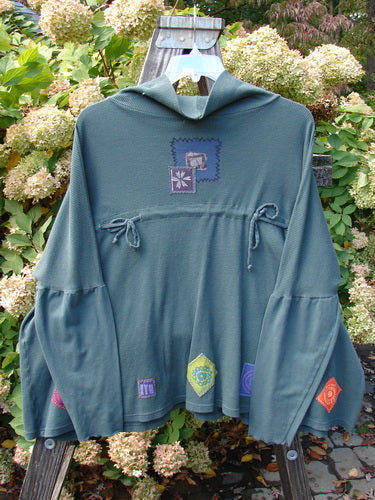 A green hooded sweatshirt with patchwork designs, featuring a flower and wood post close-ups. Barclay Patched Thermal Tie Back Cowl Top Flower Wind Army Size 3.