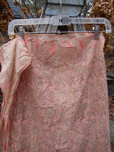 Magnolia Pearl NWT European Cotton MP Block Print Scarf Rosette drapes gracefully, showcasing its lightweight, pink-toned floral motif on sheer fabric, clipped to a clear hanger outdoors.