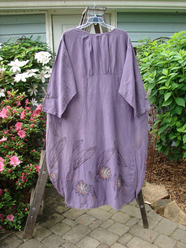 Barclay Hemp Cotton Silk Voile Belle Dress Wing Violet Size 2 displayed on a clothes hanger, showcasing its unique pleats, wide neckline, and dramatic backline with floral patterns.