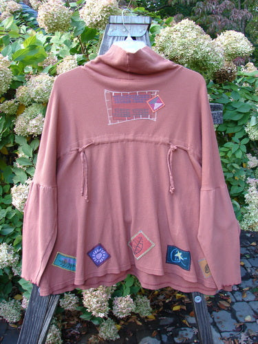 Image alt text: Barclay Patched Thermal Tie Back Cowl Top in Dusty Brick, Size 3 - Jacket with patch, pink sweater with patches, wood piece, red and blue stadium, plant, tree.