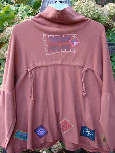 A rust thermal with a patchwork design, featuring a tie back cowl and dolmen sleeves. Size 3.