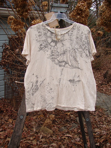 Magnolia Pearl NWT Cotton Jersey Boyfriend Tee Always & Always Moonlight OSFA hangs on a clear hanger, featuring a gray floral abstract design, draped over a ladder amidst dried foliage, reflecting casual elegance.