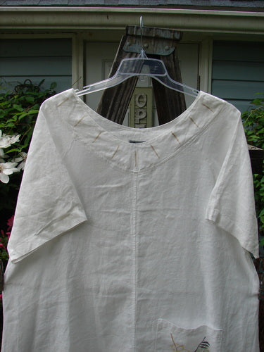 Alt text: Barclay Linen Vertical Seam Pocket Dress Leaf Dove White Size 2 displayed on a hanger, showcasing its rounded neckline, wide short sleeves, and distinctive front pocket with leaf and dove theme.