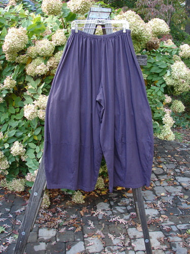A pair of Barclay 4 Square Pants in burgundy plum, made from medium-weight organic cotton. Features a unique bottom cut that creates a 3D diamond shape from the knee down. Comes with deep side pockets. Waist measures 30-40 inches, hips measure 84 inches, inseam is 25 inches, and length is 40 inches.