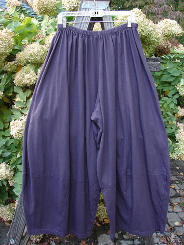 A pair of unpainted Barclay 4 Square Pants in burgundy plum, size 2, on a clothes rack. Made from medium-weight organic cotton, these pants feature a unique bottom cut that falls into a 3D diamond from the knee down. They drape and move super interestingly and come with deep side pockets. Waist fully relaxed: 30, waist fully extended: 40, hips: 84, inseam: 25, length: 40 inches.
