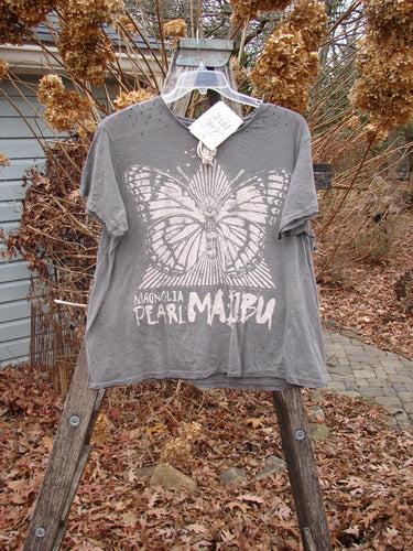 Magnolia Pearl NWT Cotton Jersey Boyfriend Tee MP Malibu Ozzy OSFA hangs on a ladder, showcasing a white butterfly graphic and text on soft gray fabric, emphasizing its drapey, distressed design.