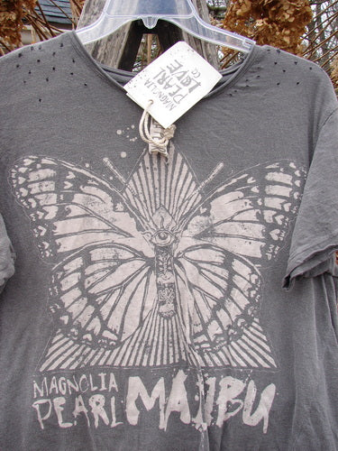 Heather-gray Magnolia Pearl NWT Cotton Jersey Boyfriend Tee MP Malibu Ozzy OSFA with stylized butterfly and sunburst graphic, hanging outdoors with visible swing tag, showcasing a drapey, distressed design.