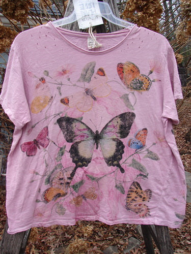Magnolia Pearl NWT Cotton Jersey Boyfriend Tee Profound Responsibility Allium OSFA, featuring butterfly motifs and a distressed look with rolled edges, hangs outdoors on a clear hanger amidst dried foliage.