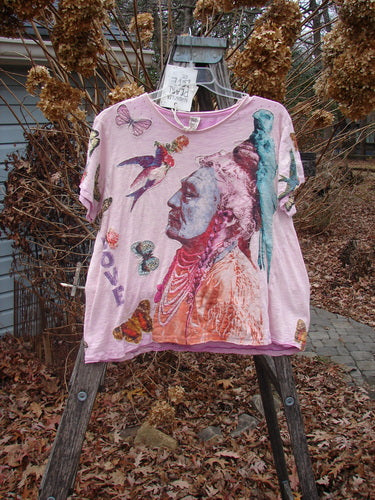 Magnolia Pearl NWT Applique Cotton Jersey Boyfriend Tee Love Is The Only Way Allium OSFA displayed on a wooden ladder, showcasing its stylized Native American figure, birds, and butterflies design amidst a natural yard setting.