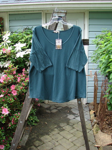 Barclay NWT Cotton Lycra Twinkle Top Unpainted Tealen Mineral Size 2 displayed on a rack, featuring a rounded, banded hemline, scooped neckline, and curly edgings on the lower sleeves.