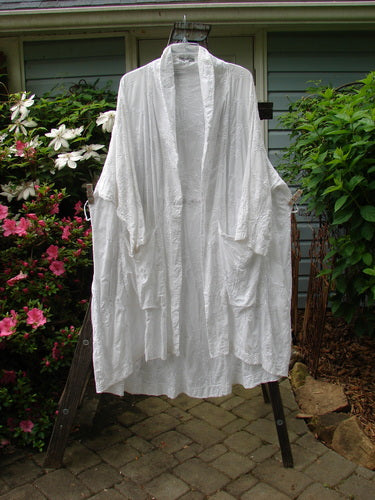 Barclay Brocade Open Front Pocket Dress Duster in White, displayed on a clothes rack. Features include drop pockets, three-quarter sleeves, varying hemline, and fold-over collar. Size 2.
