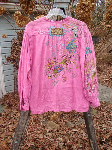 Magnolia Pearl Embroidered Linen Gypsy Johnny & Co Shirt Pinkster OSFA: A pink linen blouse with vibrant floral embroidery, billowy sleeves, and a unique rear patch, displayed on a wooden ladder outdoors.