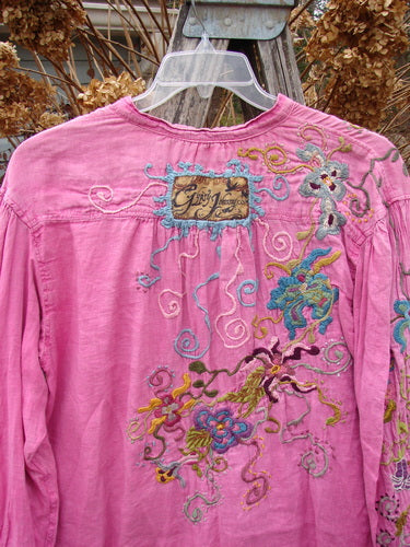 Magnolia Pearl Embroidered Linen Gypsy Johnny & Co Shirt Pinkster OSFA, featuring intricate floral and dragon embroidery, relaxed fit, billowy sleeves, and a single button front, displayed against a dried leaf backdrop.
