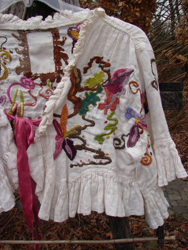 Magnolia Pearl Embroidered Linen Ruffle Ribbon Bolero White OSFA with abstract floral embroidery, ruffled edges, and a rose-pink ribbon tie, draped on an outdoor fence, reflecting Bluefishfinder.com's vintage aesthetic.