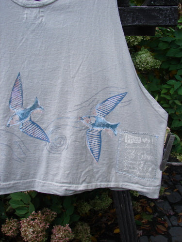 Image alt text: "1999 Pinwheel Vest Love Dove Dust Size 2: White t-shirt with birds, including a blue bird with a fish drawn on it, and a drawing of a fish. Close-ups of a wood plank and a plant."