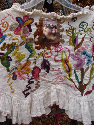 Magnolia Pearl Embroidered Linen Ruffle Ribbon Bolero White OSFA, featuring vibrant botanical embroidery, a vintage-style face patch, scalloped ruffles, and a silken ribbon closure, displayed on a hanger outdoors.