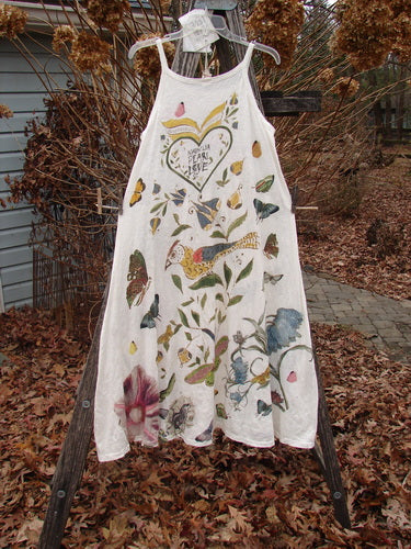 The Magnolia Pearl NWT Cotton Jersey Lana Tank Dress features hand-painted birds, butterflies, and botanicals on soft cotton, with a heart motif and script text, displayed against an autumnal outdoor setting.