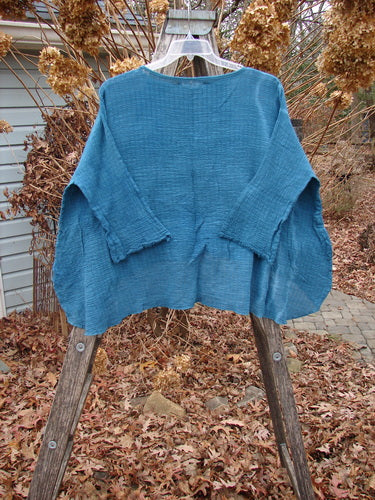 Barclay NWT Crinkle Gauze Top in mottled teal, featuring a loose, boxy cut with three-quarter dolman sleeves and a high-low hemline, displayed on a hanger outdoors against a natural backdrop.