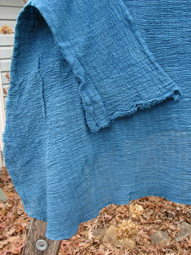 Barclay NWT Crinkle Gauze Top Mottled Teal OSFA, featuring a crinkled texture, three-quarter dolman sleeves, and a high-low hemline, draped over a wooden post with dry leaves around it.