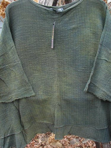 Barclay NWT Crinkle Gauze Top Mottled Evergreen OSFA, featuring a loose fit with three-quarter dolman sleeves, layered hem panels, and a slightly scooped neckline, displayed against a natural outdoor backdrop.