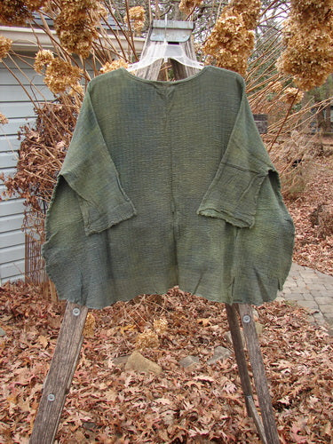 Barclay NWT Crinkle Gauze Top Mottled Evergreen OSFA draped on a ladder, showcasing its hand-woven texture, high-low hemline, and three-quarter dolman sleeves, surrounded by autumn garden elements.