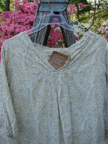 Magnolia Pearl NWT European Cotton Bondi Blouse Fleuri OSFA, displayed on a clear hanger, features a paisley print, raw-edged neckline, and pintuck plackets, set against a garden backdrop.
