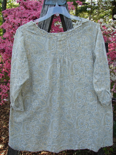 Magnolia Pearl NWT European Cotton Bondi Blouse Fleuri OSFA displayed outdoors, showcasing its wide neckline, relaxed sleeves, and raw edges, with delicate paisley print against a lush garden backdrop.